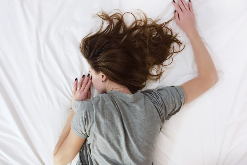 Brunette girl sleeping in a grey shirt on white bedsheets